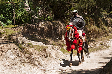 A man riding a horse with traditional red and yellow Ethiopian headdress and carrying a traditional round shield, Ethiopia, Africa