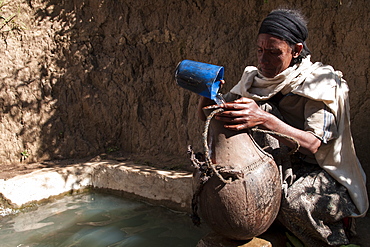 A woman fills a traditional water pot from a capped spring, Ethiopia, Africa