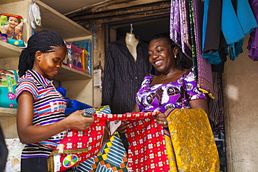 A female shopkeeper showing different colourful materials to a potential customer, Nigeria, West Africa, Africa