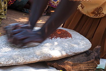 A woman using two stones to grind grain in to flour, Uganda, Africa