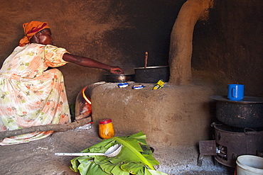 A woman cooking on a fuel efficient stove inside a traditional mud hut kitchen, Uganda, Africa