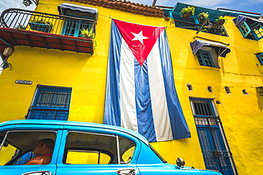 Old American classic car and huge Cuban flag on yellow building in Havana, La Habana (Havana), Cuba, West Indies, Caribbean, Central America