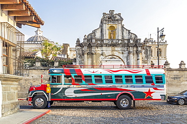 A typical colorful painted chicken bus passing at the entrance gate of San Francisco Church in Antigua, UNESCO World Heritage Site, Guatemala, Central America