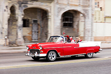 Red and white vintage American taxi driving along the Malecon, Havana, Cuba, West Indies, Caribbean, Central America