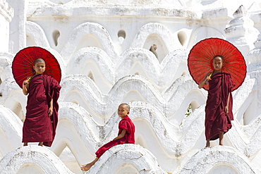 Three young monks dressed in red, with red parasols at the Myatheindan Pagoda (White Temple) in Mingun, Myanmar (Burma), Asia