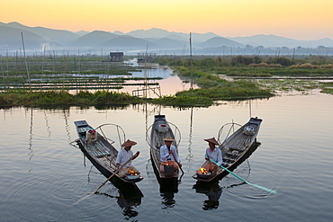 Three fishermen keep warm in their long tail fishing boats at dawn near the floating gardens on Inle Lake, Shan State, Myanmar (Burma), Asia