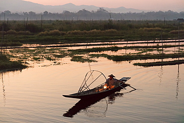 A fisherman keeps warm in his long tail fishing boat at dawn near the floating gardens on Inle Lake, Shan State, Myanmar (Burma), Asia