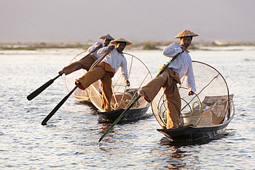 Three fishermen row with one leg at sunset on Inle Lake, Shan State, Myanmar (Burma), Asia