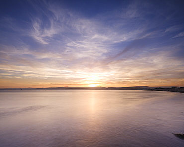 With interesting wispy clouds, the sun sets across the water from Exmouth, Devon, England, United Kingdom, Europe