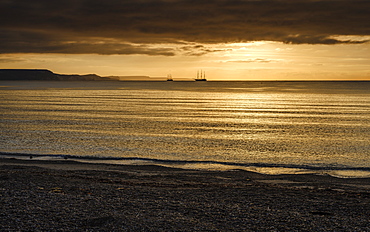 Two square rigger sailing vessels at anchor on a shimmering sea, adjacent to the Jurassic Cliffs, Weymouth, Dorset, England, United Kingdom, Europe