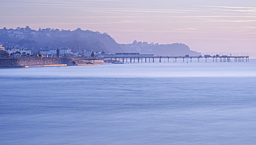 Sun making the sea wall glow on Teignmouth sea front with Teignmouth Pier behind, viewed from Shaldon, Devon, England, United Kingdom, Europe