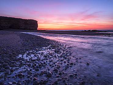 The River Otter meets the sea with strong dawn colour, wet pebbles and the cliff of Otter Head at Budleigh Salterton, Devon, England, United Kingdom, Europe