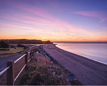 Colourful dawn with sweep of the shoreline, beach huts, pebbles and the cliff of Otter Head at Budleigh Salterton, Devon, England, United Kingdom, Europe