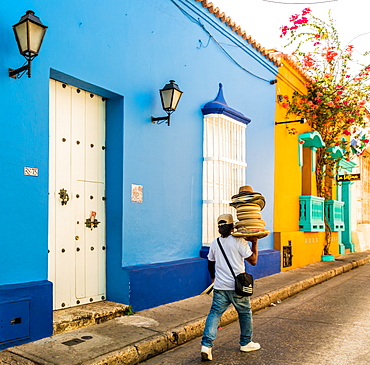 A street vendor walking past a colourful building in the old town in Cartagena, Colombia, South America