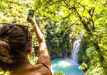 A tourist taking a picture of the Rio Celeste waterfall in Tenorio Volcano National Park, Costa Rica, Central America