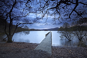 A solitary figure at dusk on Rigg Wood jetty, Coniston Water, Lake District National Park, UNESCO World Heritage Site, Cumbria, England, United Kingdom, Europe