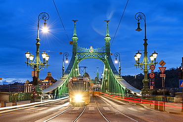 Trams crossing Liberty Bridge illuminated at night with the Gellert Hotel in the background, Budapest, Hungary, Europe