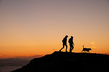 Silhouette of man and woman with dog at sunrise, Winnat's Pass, The Peak District, Derbyshire