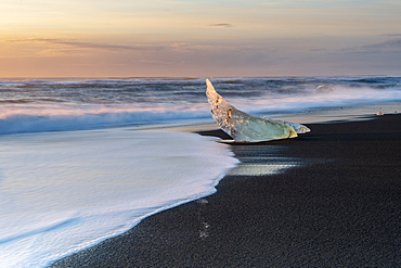 Glacier ice on black sand beach with waves crashing up the beach, near Jokulsarlon, South Iceland, Iceland, Polar Regions