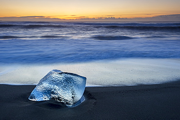 Glacier ice on black sand beach with waves washing up the beach on a winter day, near Jokulsarlon, South Iceland, Iceland, Polar Regions