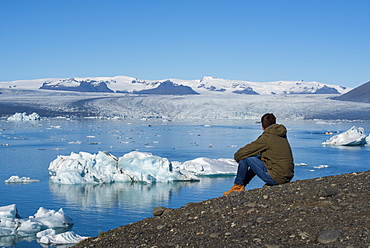 Young male sat admiring the view of Jokulsarlon Glacier Lagoon, South East Iceland, Iceland, Polar Regions