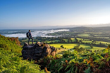 A walker stood on a rock at Cloudside looking across the Cheshire Plains, Congleton, Cheshire, England, United Kingdom, Europe