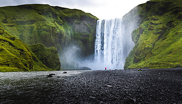 Visitor dwarfed by plunging waters of Skogafoss, Iceland's most iconic waterfall, situated on the Skoga River, Southern Region, Iceland, Polar Regions