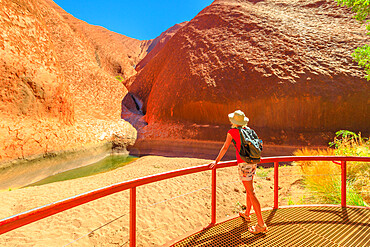 Tourist woman with wide hat standing at balcony admiring Mutitjulu Waterhole at the end of short Kuniya walk in Uluru-Kata Tjuta National Park, UNESCO World Heritage Site, Northern Territory, Australia, Pacific