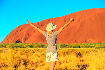 Carefree tourist woman with raised arms enjoys Uluru (Ayers Rock) at sunset in Uluru-Kata Tjuta National Park, UNESCO World Heritage Site, Northern Territory, Australia, Pacific