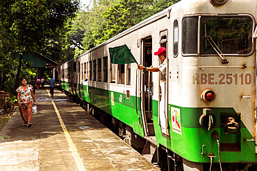 A passenger train at Lanmadaw station with train conductor waving a green flag and a passenger on the platform, Yangon (Rangoon), Myanmar (Burma), Asia