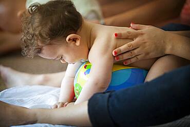 Baby massage lesson with a certified masseur, a young mother learns how to massage her 1-year old son.