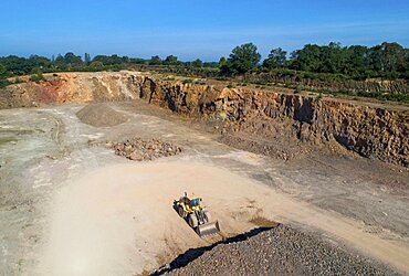 Aerial view of a digger in a quarry in front of a pile of rubble.