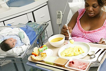 Mother having meal in maternity hospital, her newborn baby beside