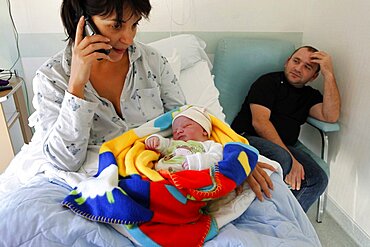 Mother using telephone with father and newborn in hospital