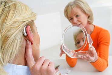 Woman holding mirror for other woman trying hearing aid