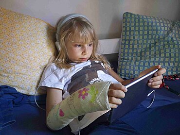 8 year old girl with broken, plastered wrist, watching a cartoon on a touch pad, European, France.