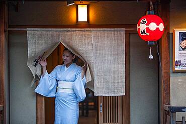 woman inviting passersby to enter into her restaurant.