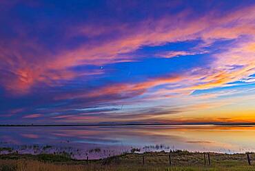 Sunset colours over Deadhorse Lake in southern Alberta, on July 8, 2016. The waxing crescent Moon shines amid the colourful clouds.