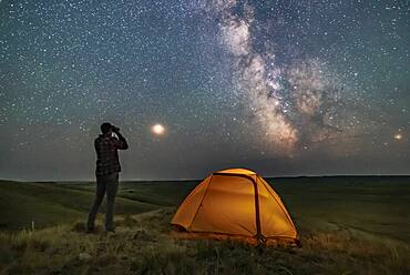 A Park interpreter poses for a scene in Grasslands National Park, Saskatchewan, of stargazing with binoculars under the Milky Way on a dark moonless night. Grasslands is perfect for stargazing as it is a Dark Sky Preserve and the horizon is vast and unobstructed.