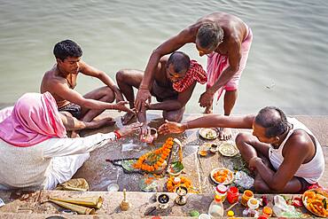 Pilgrims making a ritual offering and praying, ghats of Ganges river, Varanasi, Uttar Pradesh, India.