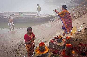 Pilgrims making a ritual offering and praying, ghats of Ganges river, Varanasi, Uttar Pradesh, India.