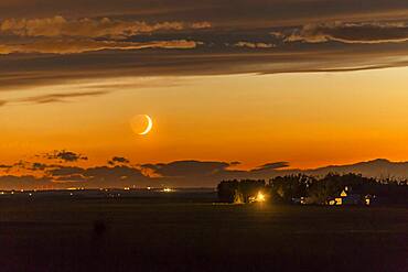 The waxing crescent Moon setting over a nearby farm, on June 26, 2017. Shot at the start of a time-lapse sequence, and shot in haste from home as the Moon appeared from beneath an otherwise very cloudy sky. The dark side of the Moon is lit by Earthshine, prominent despite the Moon's low altitude and bright twilight sky.