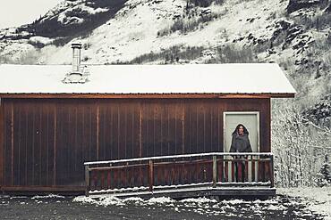 A young Woman is wrapped in a woolen blanket outside of a simple wooden cabin. Yukon Territory, Canada