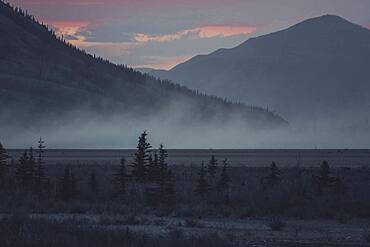 The sky is glowing softly as the sun sets behind the mountains of the Kluane National Park. Yukon Territory, Canada