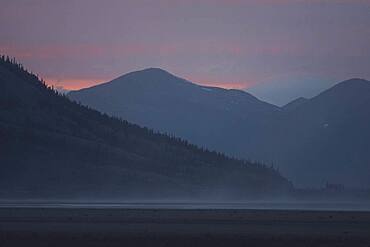 The sky is glowing softly as the sun sets behind the mountains of the Kluane National Park. Yukon Territory, Canada