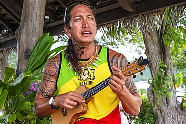 Local tattooed person playing the ukulele in Huahine, Society Islands, French Polynesia, South Pacific.