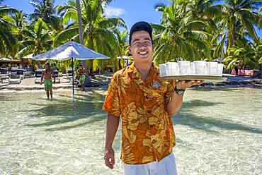 A waiter serves cocktails in Taha'a island resort, French Polynesia. Motu Mahana palm trees at the beach, Taha'a, Society Islands, French Polynesia, South Pacific.