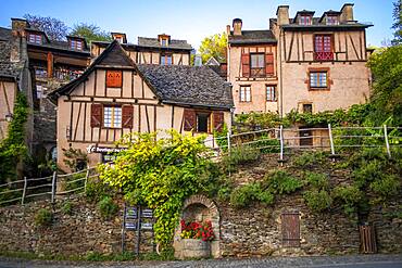 The small medieval village of Conques in France. It shows visitors its abbey-church and clustered houses topped by slate roofs.  Crossing of narrow streets and monolith to the fallen ones in the war in the old medieval village of Conques on coats of the river Dordou