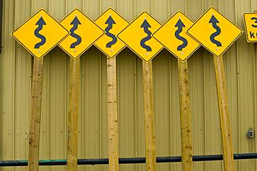 Roadside curve signs leaning on public works building.