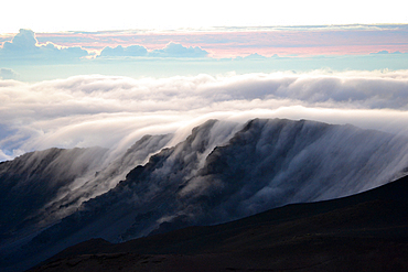 Clouds over a mountain edge at the summit of Haleakala volcano during sunrise, Maui, Hawaii, USA